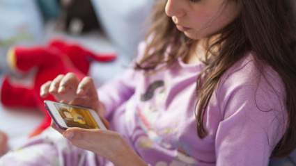 Una niña juega juegos en un dispositivo móvil en la cama