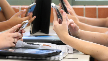 2D9CTNT 2D9CTNT Students holding and using a range of digital devices. Mobile cell phones tablets and technology being handled by students at a desk in a school educa