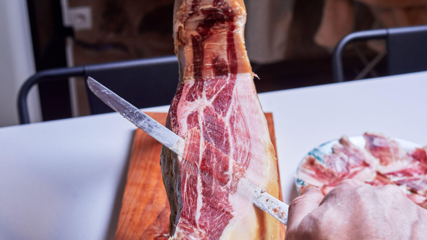 Una mano de un cortador de jamón profesional cortando un jamón ibérico en finas lonchas listo para comer