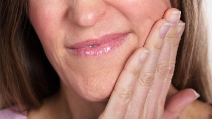 Mujer presionando su mejilla magullada con una expresión de dolor