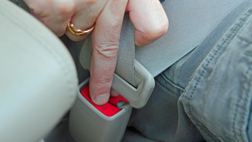 La mano de un hombre desbloqueando el cinturón de seguridad de un coche.