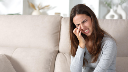 Mujer quejándose de rascarse el ojo sentada en un sofá en casa