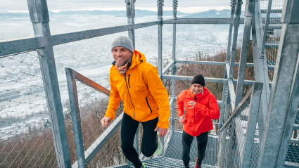 Dos hombres vestidos con ropa deportiva de color rojo y amarillo brillante subiendo enormes escaleras industriales de acero en un frío día de invierno.