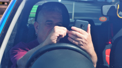 Un hombre de mediana edad estaba sentado en un automóvil estacionado sosteniendo y mirando un teléfono móvil y concentrándose