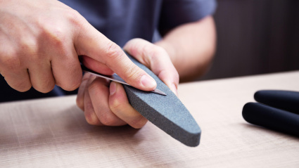 Manos masculinas fuertes afilan un cuchillo de cocina de metal con una piedra de afilar. Afilado de cuchillos doméstico.