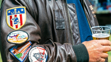 Patriota estadounidense bebiendo cerveza y vistiendo una chaqueta bomber de cuero con calcomanías en la manga.
