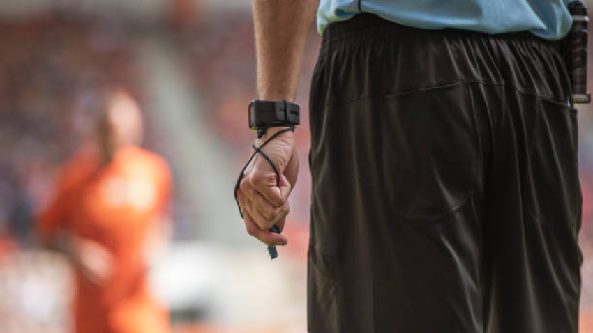 Hand of soccer referee with wristwatch and whistle