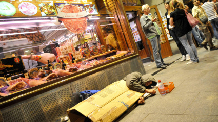 Un hombre sin hogar duerme en una acera cerca de una cafetería en el centro de Madrid