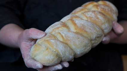 Panadería: pan horneado en horno de leña. Panadero con un pan trenzado en las manos.