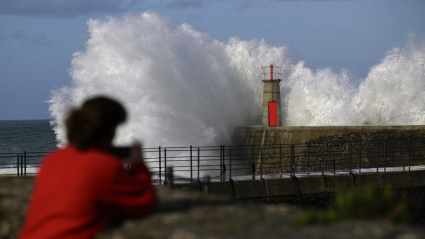 Una ola rompe en el puerto de Viavélez (Asturias), mientras una persona fotografía el momento