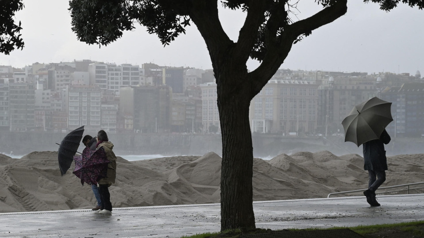 Varias personas se protegen de la lluvia junto a la costa de A Coruña