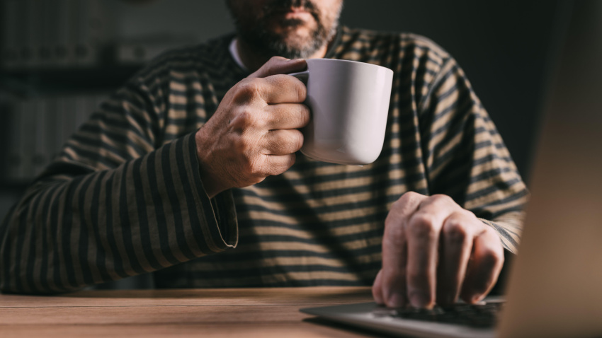 Trabajador autónomo que trabaja con un ordenador portátil en su oficina en casa a altas horas de la noche y toma café para mantenerse despierto