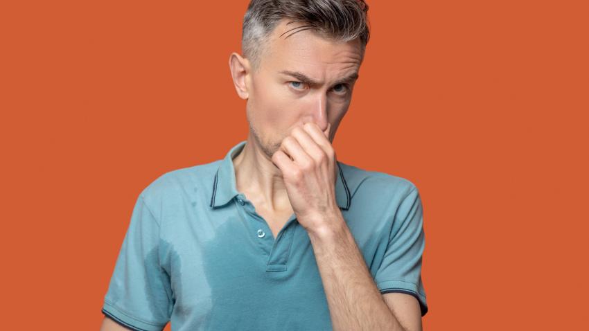 Hombre con camisa con manchas húmedas tocándose la nariz