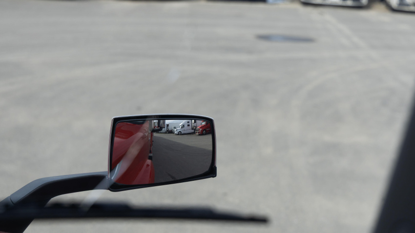 Un camión está estacionado y su espejo lateral refleja varios otros camiones y vehículos estacionados en un estacionamiento.
