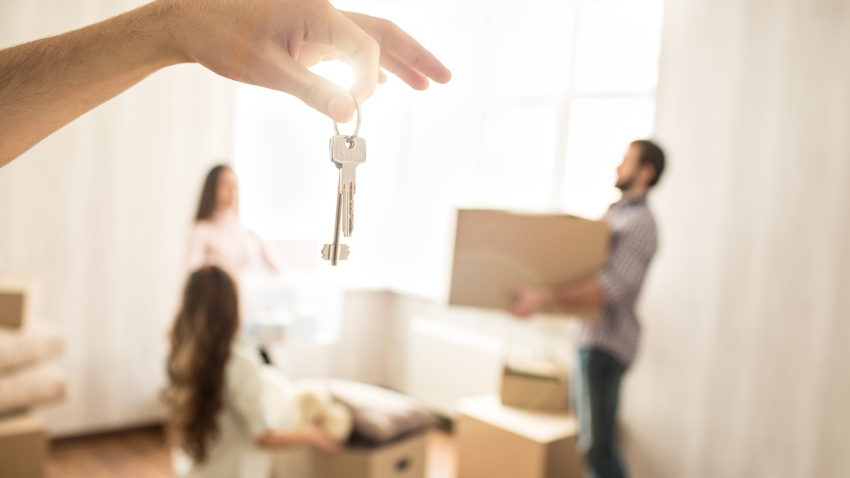 Nice picture of family working together. Man and woman are holding boxes while their child wants to help them. THere is a hand with set of keys in front of the picture
