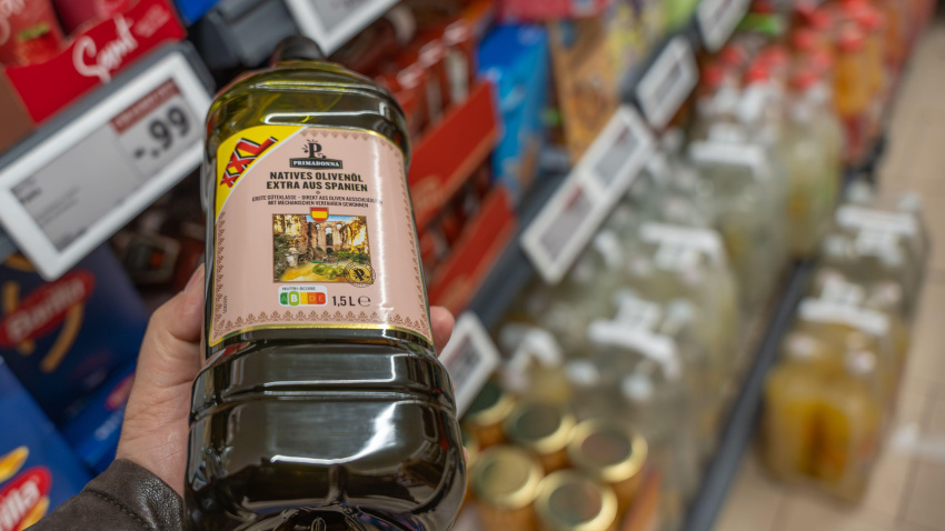 Mano sosteniendo una botella grande de aceite de oliva virgen extra en el pasillo de un supermercado