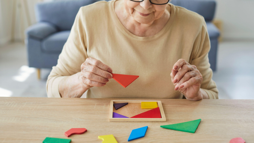 Mujer mayor sentada en la mesa resolviendo un rompecabezas de madera