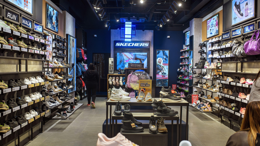 Interior de una moderna tienda minorista de Skechers que exhibe diversas zapatillas y zapatos deportivos en los estantes de un centro comercial.