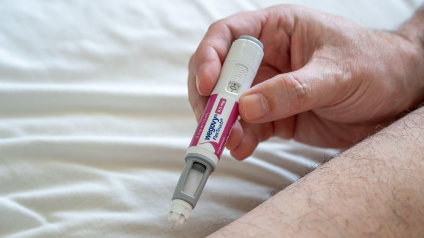 Hombre usando una pluma de inyección Wegovy para bajar de peso, administrando una dosis subcutánea en el muslo. Concepto de atención médica y control de la obesidad.