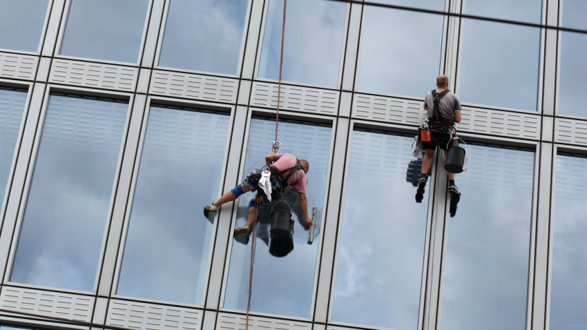 Dos técnicos en trabajo vertical limpian ventanas en un edificio de oficinas.