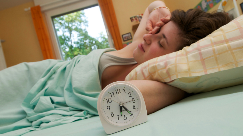 Joven despierta pronto en su cama con el despertador y se frota los ojos