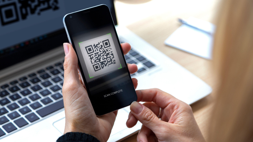 Mujer con un teléfono móvil en la mano escaneando un código QR desde la pantalla de un ordenador portátil