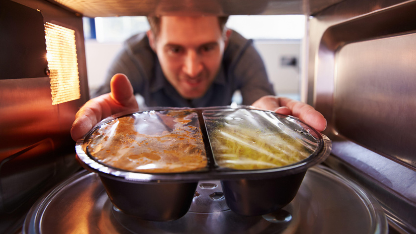 Imagen de recurso de un hombre metiendo un plato de comida preparada en el microondas