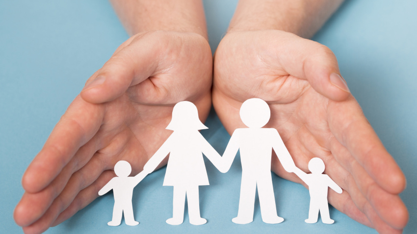 Dos manos protegen a siluetas de papel que representan familias e infancia
