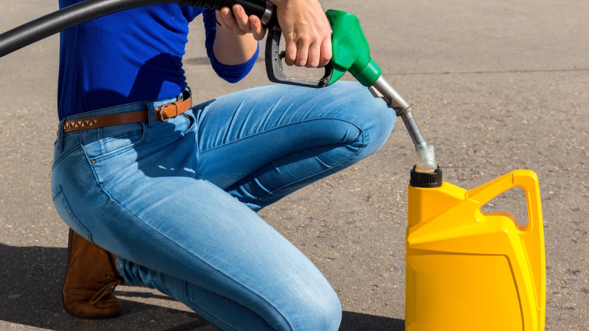 Mujer joven llenando una garrafa amarilla con una manguera de gasolina al aire libre