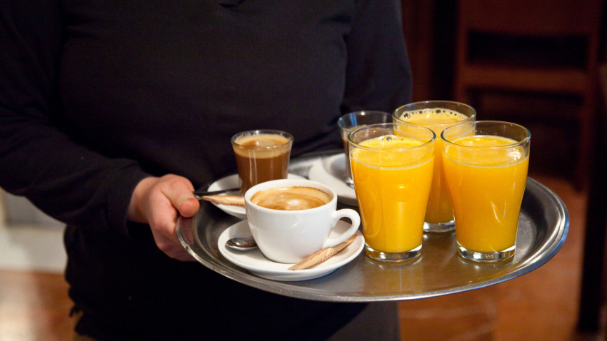 Imagen de recurso de un camarero sirviendo un desayuno con varios zumos de naranja