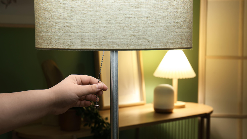 Mujer encendiendo una lámpara de pie en una sala de estar oscura.