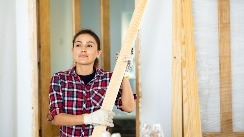 Mujer transportando tablones de madera durante trabajos de reforma en una obra