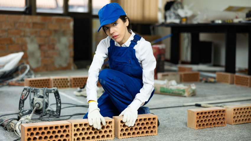 Una mujer albañil coloca ladrillos dentro de un edificio en construcción.