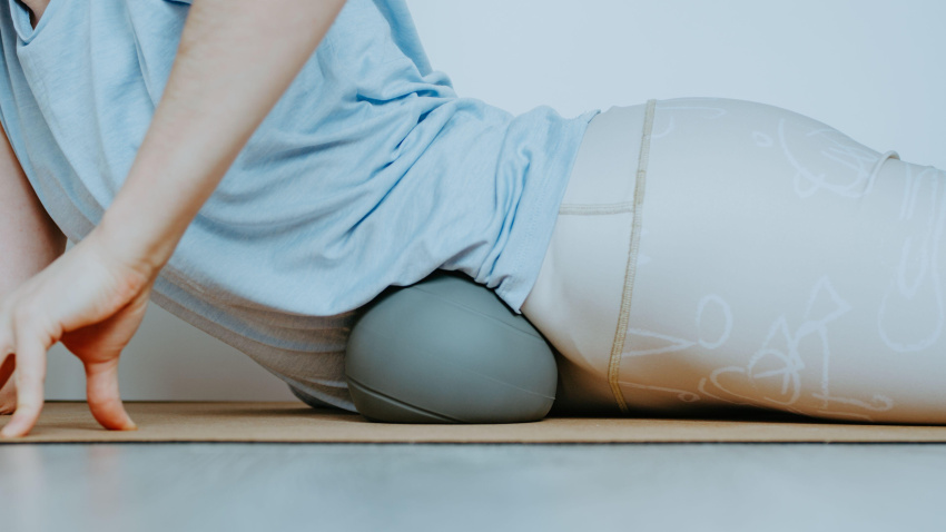 Mujer realizando una liberación miofascial visceral sobre una pelota gris suave. Concepto: prácticas de autocuidado en casa.
