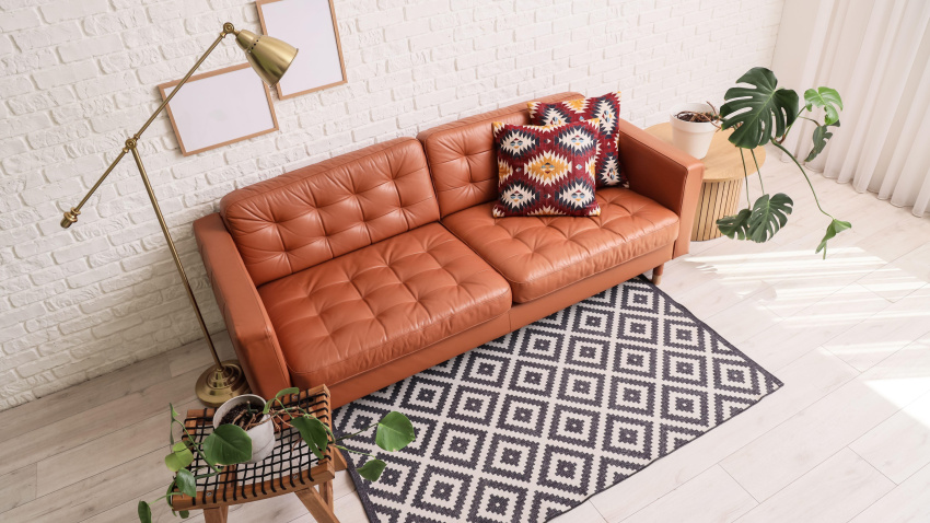 Interior de la sala de estar con sofá de cuero, lámpara y plantas de interior Monstera verdes sobre mesas de centro cerca de una pared de ladrillo blanco.