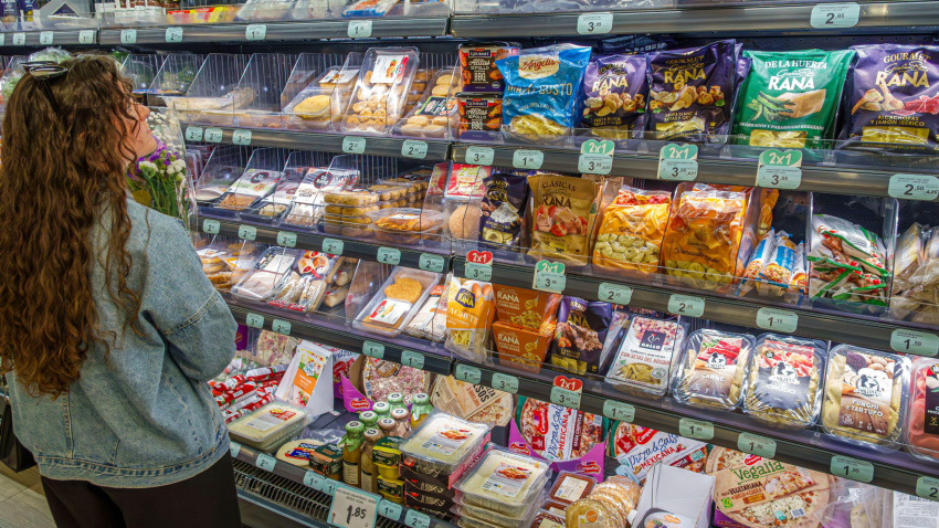 Una mujer frente a un estante del supermercado con comida preparada