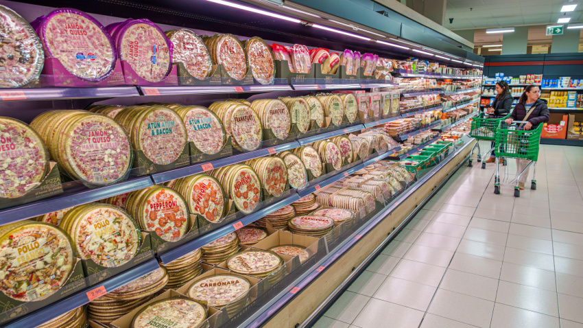 Varias personas con carritos de la compra en un supermercado frente a estantes con comida preparada