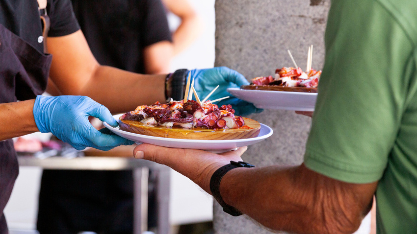 Un chef anónimo, con guantes, entrega un plato de tapas de pulpo recién preparadas a un cliente.