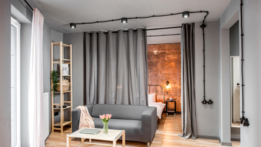 Salón moderno de estilo loft en tonos grises con sofá y dormitorio detrás de las cortinas.