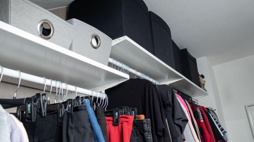 Armario organizado con ropa y cajas de almacenamiento en la parte superior.