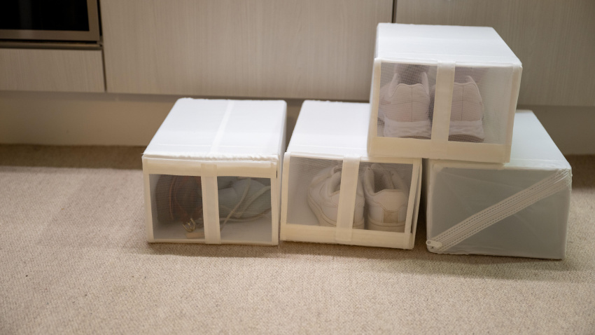 Concepto de organización minimalista del hogar con cajas de almacenamiento de zapatos de tela blanca apiladas ordenadamente en el suelo.
