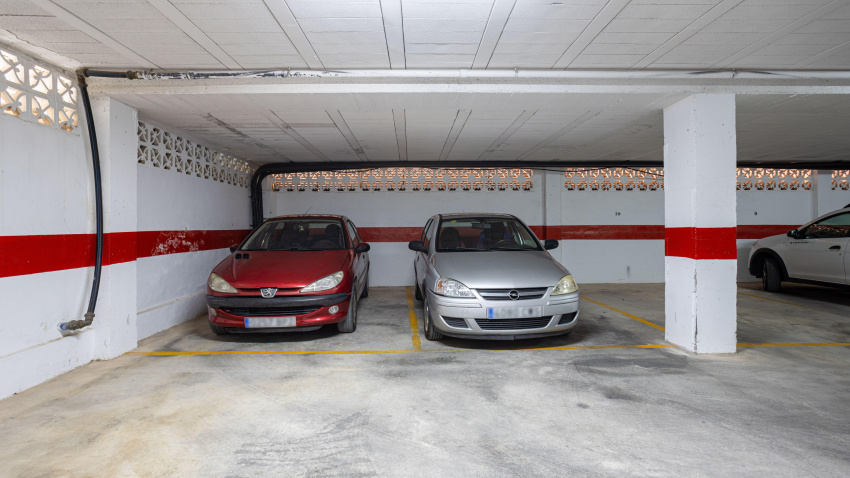 Garaje cubierto con coches aparcados y una franja roja pintada en las paredes de hormigón.