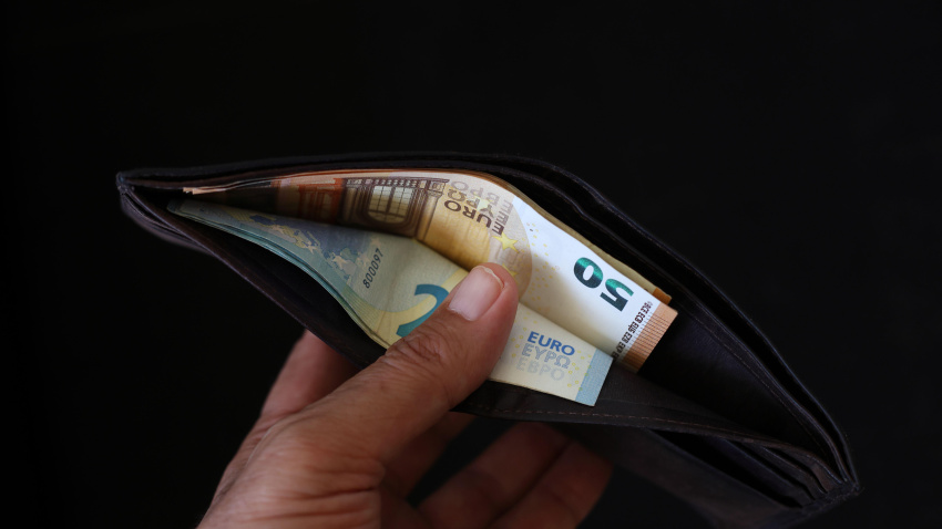 Dinero en una cartera sobre fondo negro. Mano mostrando una cartera abierta con euros.