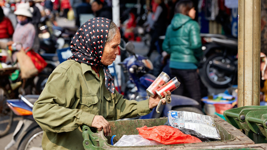 Una mujer clasifica un contenedor verde en busca de artículos reutilizables en un mercado concurrido de Hanói durante el día en Hanoi