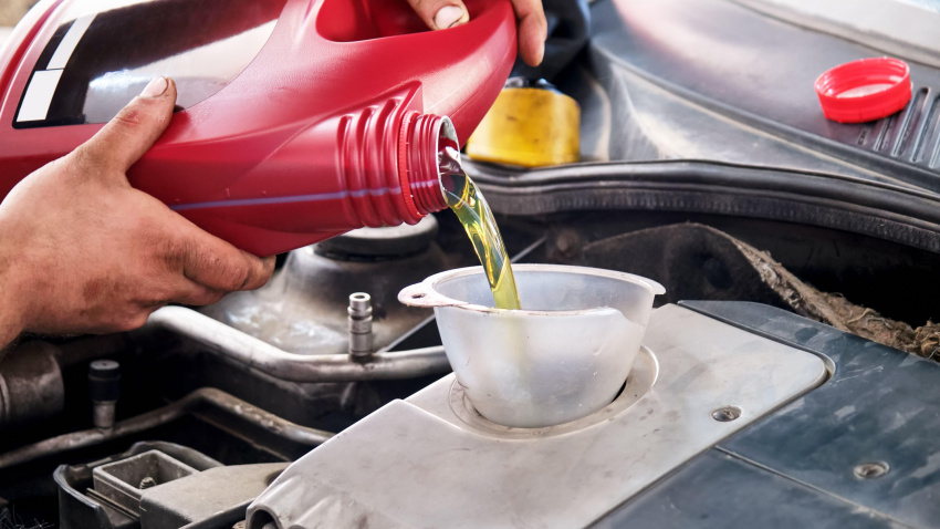 Manos de un mecánico añadiendo o vertiendo aceite al motor del coche.