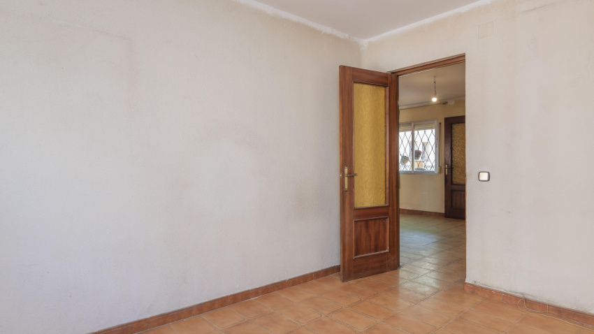 Una pequeña habitación con paredes de gotele y suelos de gres blanco, marrón mal pintados y una puerta de madera de sapeli con cristal