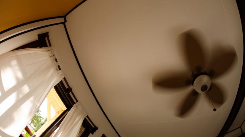 Cortinas con ventilador de techo en la ventana, meciéndose con la brisa en la habitación del hotel El Pescador.