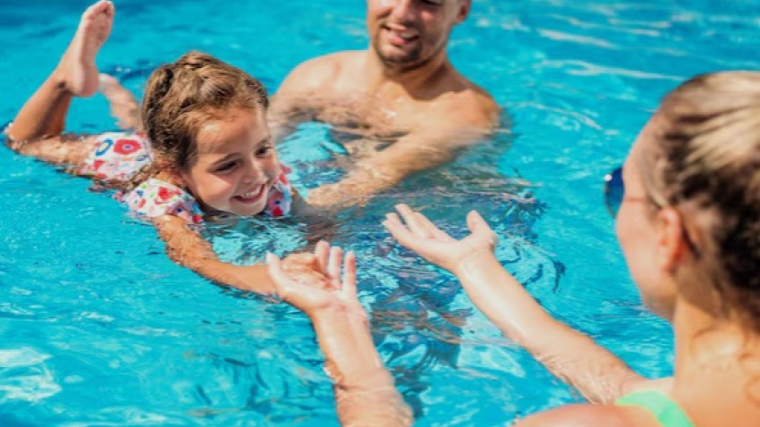 Unos padres con su hija nadando dentro de la piscina