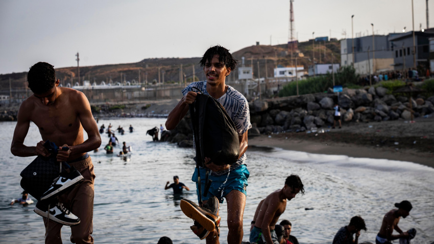 Los migrantes se congregan cerca del paso fronterizo de Tarajal en Ceuta mientras las fuerzas de seguridad españolas vigilan la zona durante la tarde.