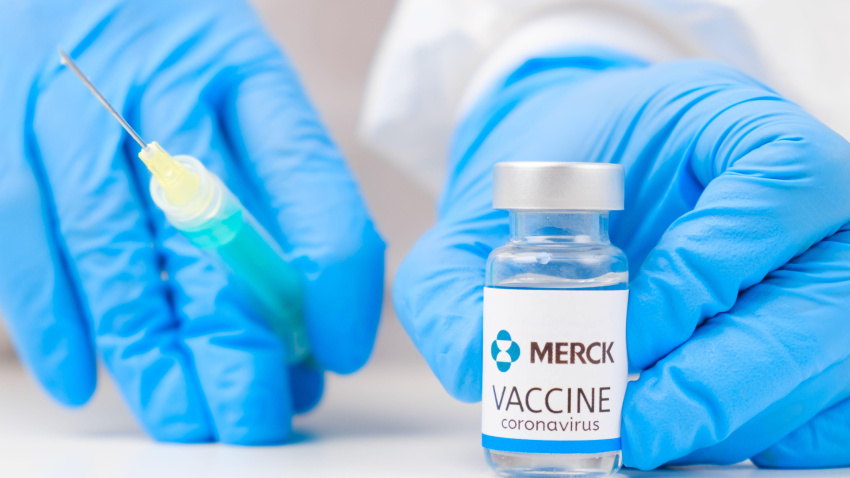 Vacuna Merck contra el coronavirus y jeringa para inyección en la mano de un trabajador sanitario con guantes de goma y traje protector.